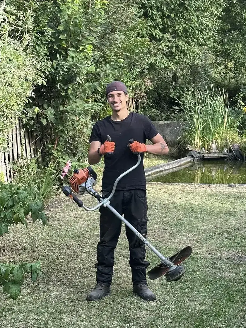 Robert Everson dans un jardin, débroussailleuse à la main.